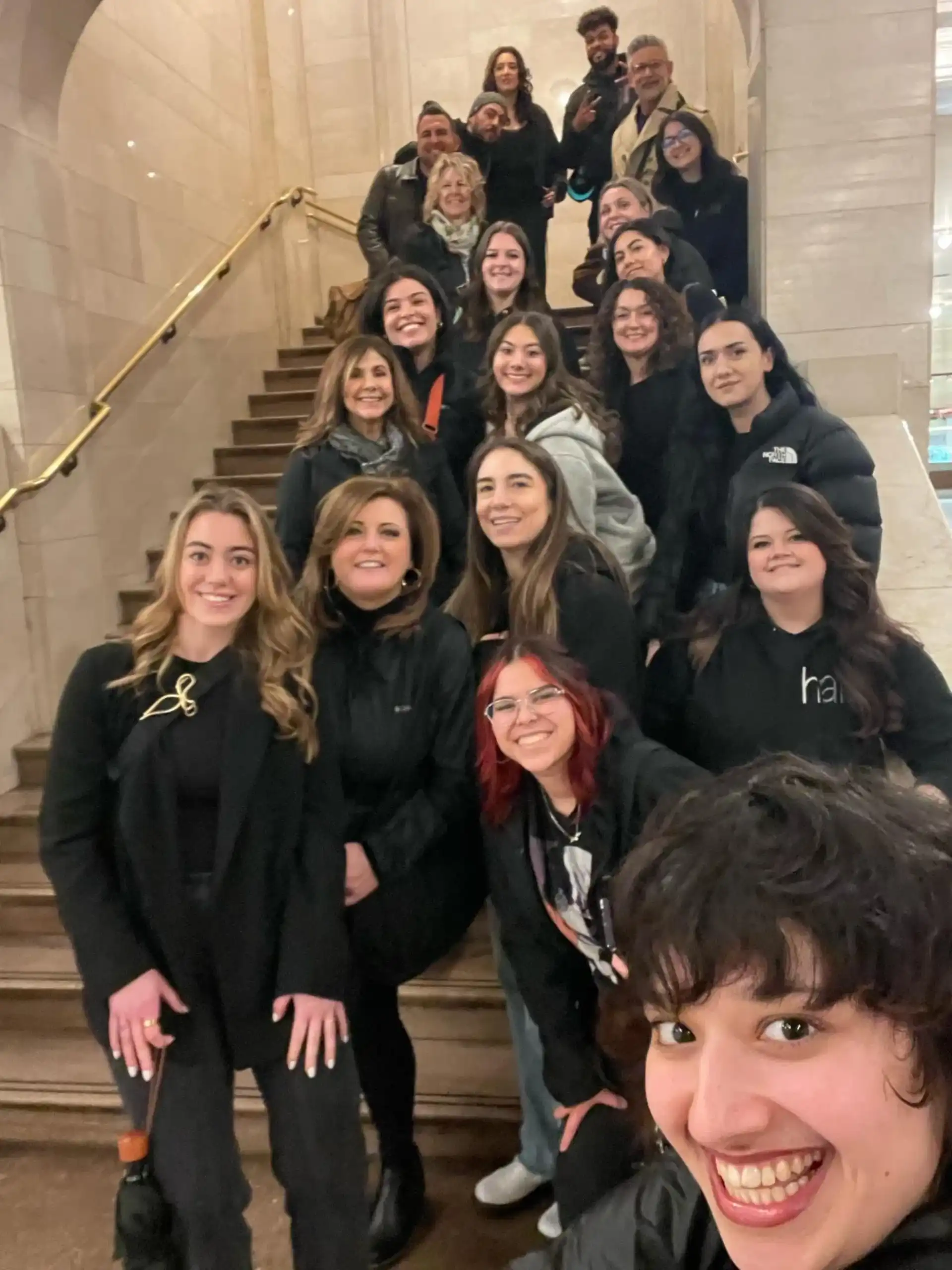 Group of people smiling on a staircase, with one person in front taking a selfie.